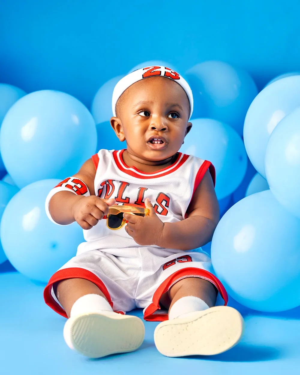 Baby in a basketball outfit surrounded by blue balloons