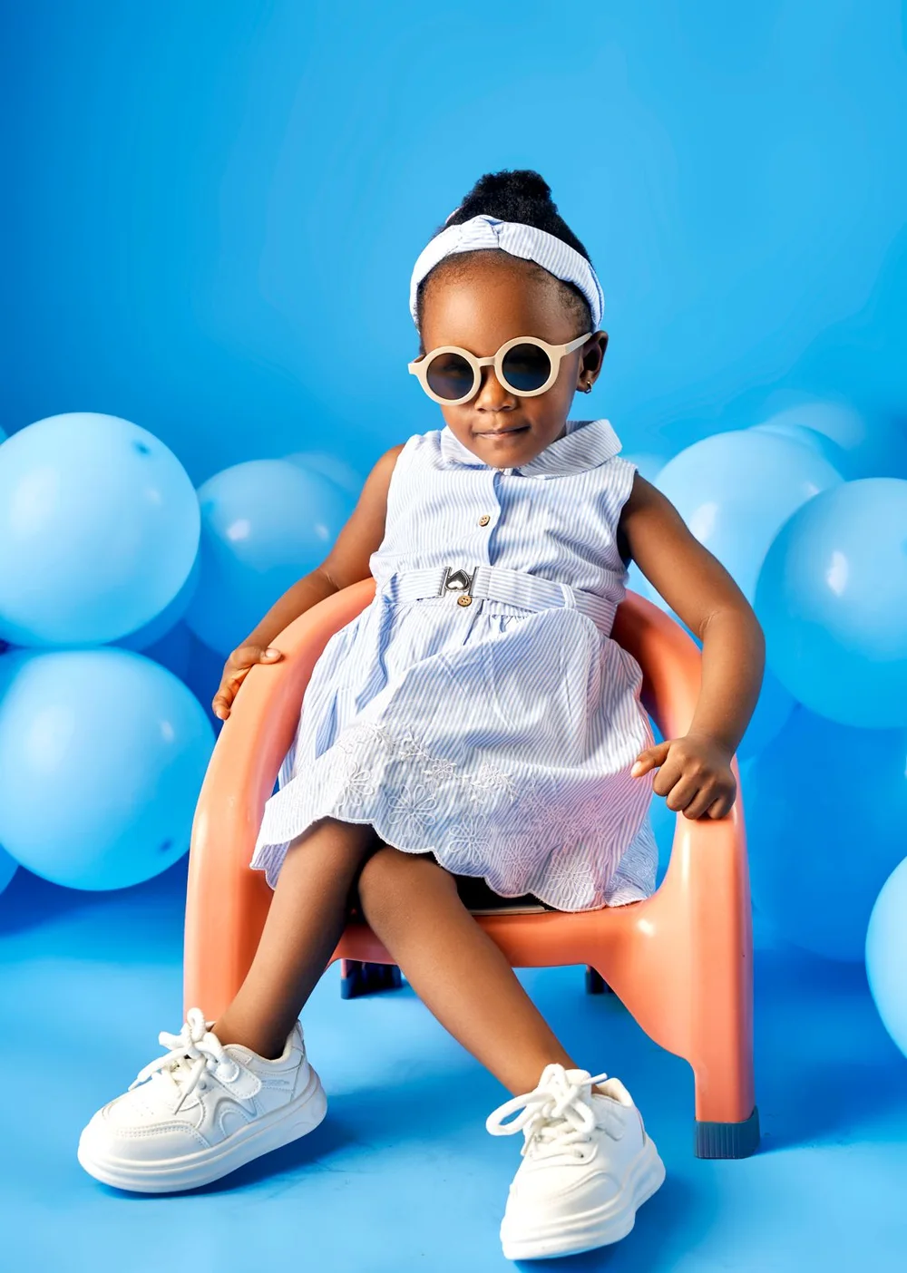Girl in a striped dress sitting on an orange chair